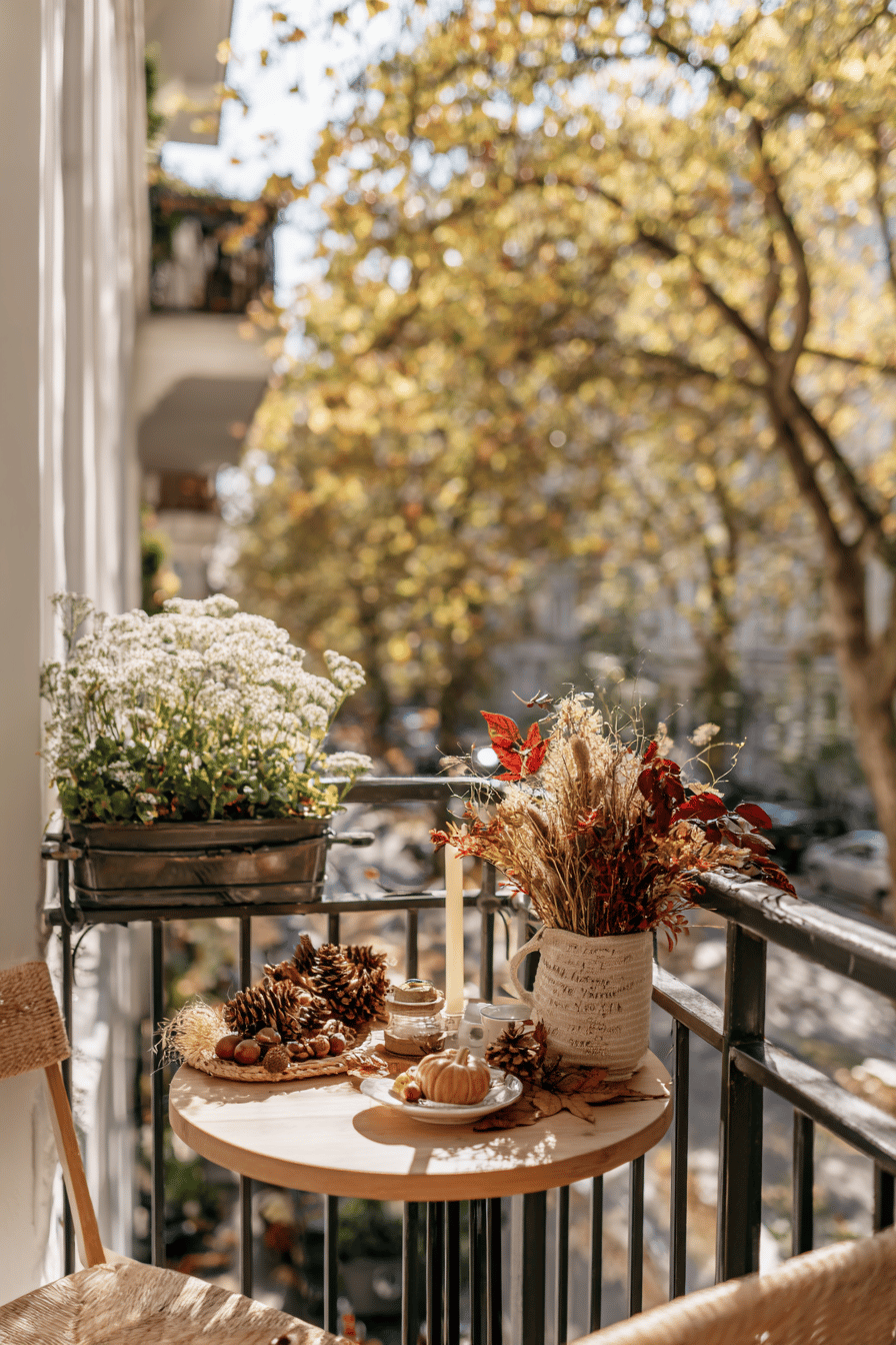 Herbstlich dekorierter Balkon mit Kranz aus Blättern, Tannenzapfen und Hagebutten, kleinen Kürbissen und einer Laterne auf einem Holztisch.