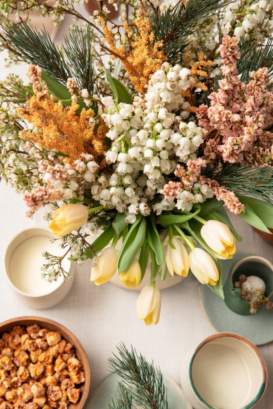 Frischer Blumenstrauß mit weißen Tulpen, Maiglöckchen, Tannenzweigen und Trockenblumen auf gedecktem Tisch