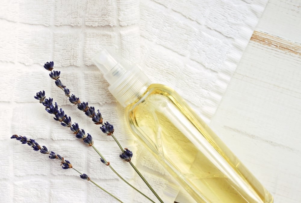 Sprühflasche mit Lavendel-Wäschespray neben Bettwäsche
