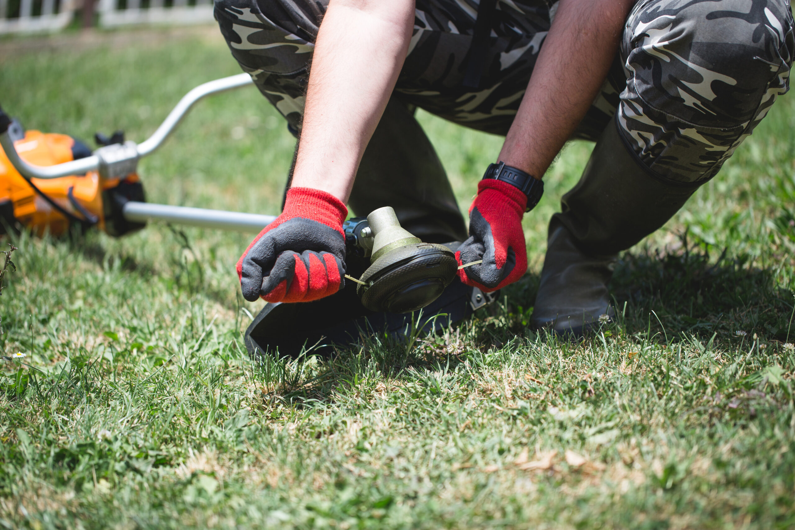 Person richtet Rasentrimmer im Gras.