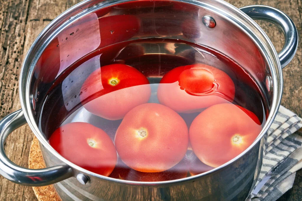 Tomaten liegen in einem Topf mit Wasser, um die Haut zum Ablösen zu bringen