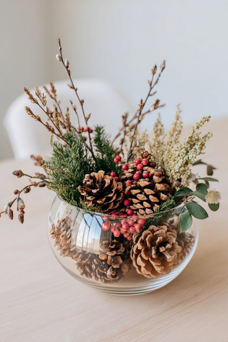 Glasvase mit Tannenzapfen, roten Beeren und Zweigen als Winterdeko